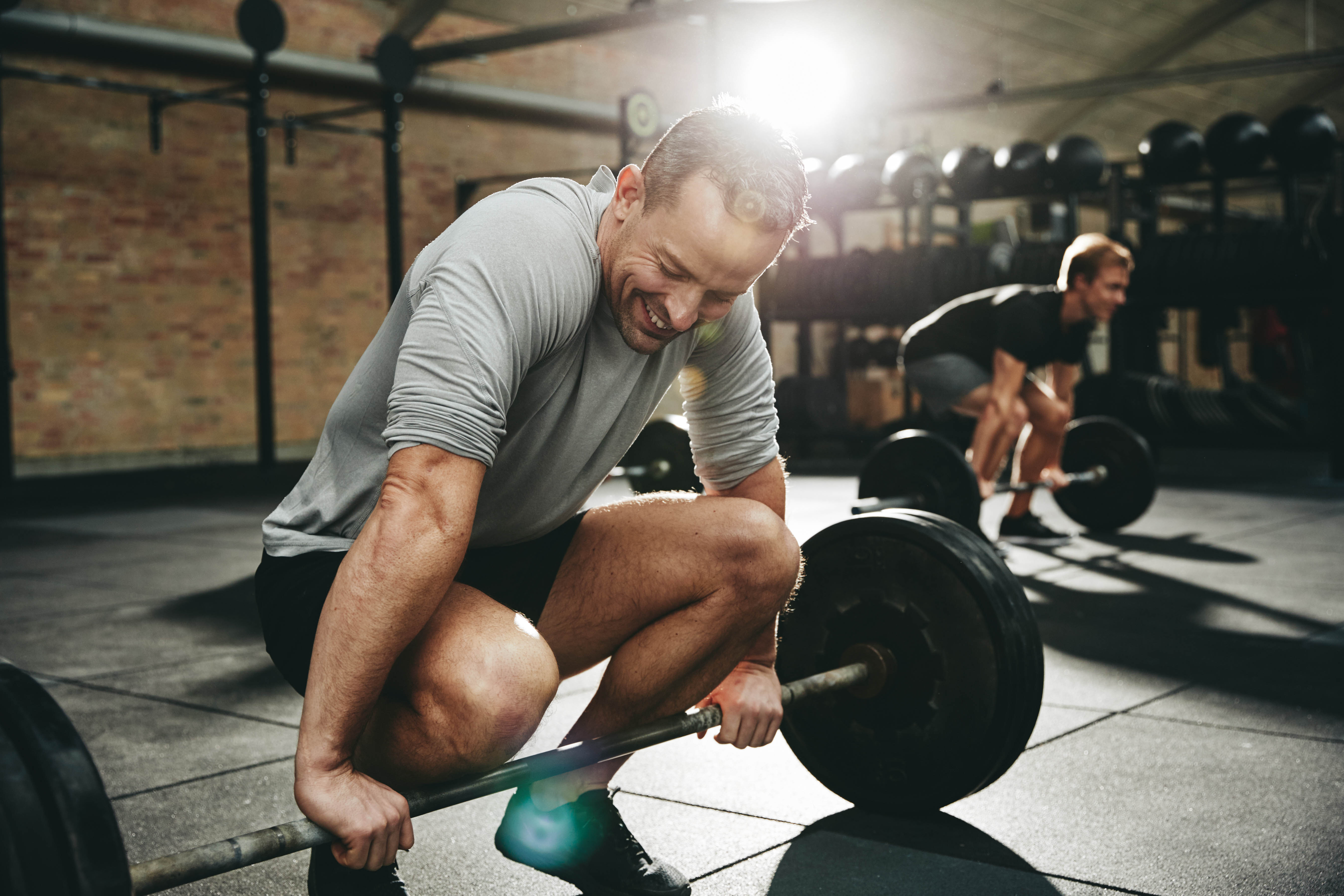 Fit man smiling while crouched down beside a barbell during a workout class at the gym